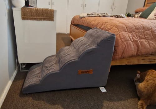 Customer's grey foam dog stairs placed in a bedroom next to a bed.