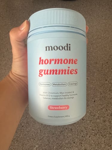 Reviewer holding a light blue bottle of Moodi hormone gummies in the Strawberry flavor.