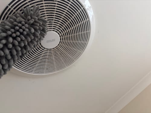 Customer using the grey Koala Extendable Duster to clean dust from a round ceiling vent.