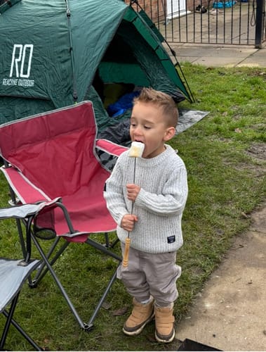 Customer's green 3 Secs Tent pitched on grass, with a young child eating a marshmallow in the foreground.