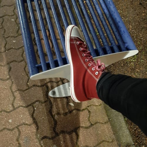 Ein Rezensent trägt den roten Roam I - Barfußschuh mit weißer Sohle auf einer Bank.