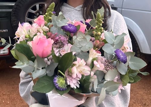 Customer holding the Harmony Flower Arrangement, a lush bouquet with pink roses and purple blooms.