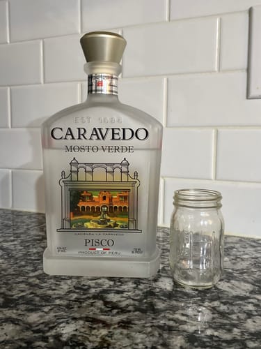 Customer's frosted bottle of Caravedo Mosto Verde Pisco on a counter next to a small glass.