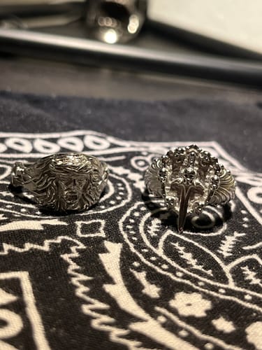 Reviewer's detailed Sword & Shield Ring shown on a patterned cloth next to another silver ring.