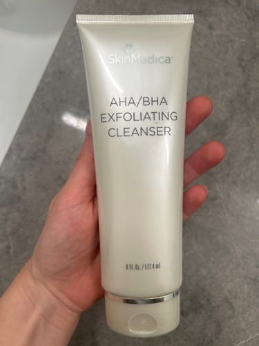 Customer holding a pearl-white tube of SkinMedica AHA/BHA Exfoliating Cleanser in their hand.