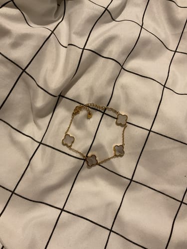 Rezensentin zeigt das goldene Weiße Kleeblatt Armband auf einem Stoff mit Gittermuster.
