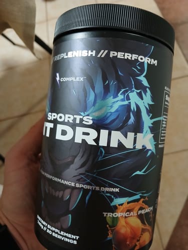 Reviewer holding the black tub of Sports Iont Drink in the Tropical Peach flavor.