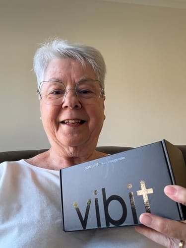 A happy reviewer holding the black and gold box for the Vibit ROLL portable vibrating massage roller.