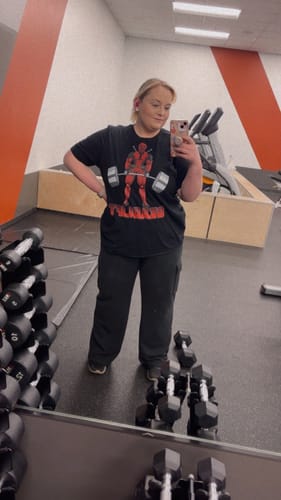 Reviewer in a gym taking a mirror selfie to show the fit of their black Deadlift T-Shirt.