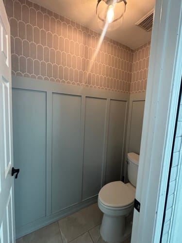 Customer's Felix Wallpaper installed above light blue wainscoting in a small bathroom, as seen from the doorway.