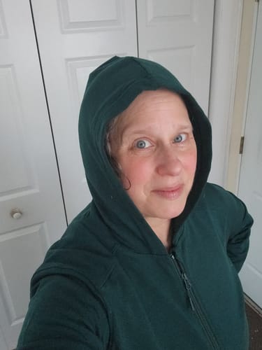 Reviewer wearing the Darby Zip Up Hoodie in Deep Timber with the hood up indoors.