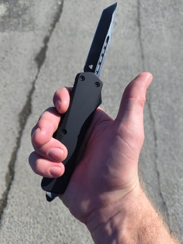 Customer holding their black Ghost OTF Knife with the blade extended.