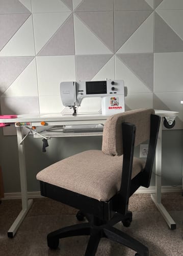 Customer's beige upholstered Arrow Hydraulic Sewing Chair positioned in a sewing room in front of a white table.
