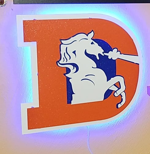 Customer's Denver Broncos metal wall art, backlit with blue LED lights and mounted on a wall.