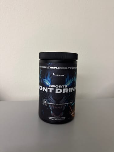 Customer's black tub of Sports Iont Drink powder shown on a plain surface.