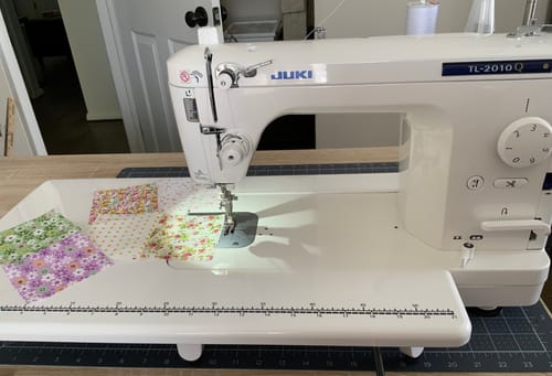 Customer's Juki TL-2010Q quilting machine with its auxiliary table, sewing several small, colorful fabric squares.