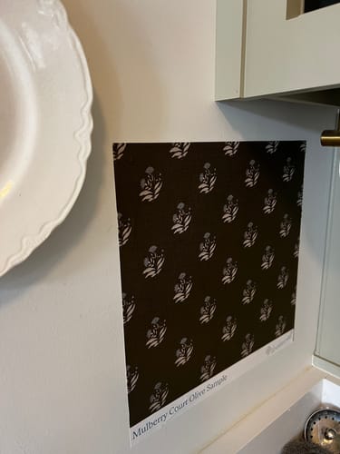 Customer's Mulberry Court Wallpaper sample in a dark olive color with a floral pattern, shown stuck to a white wall in a kitchen.