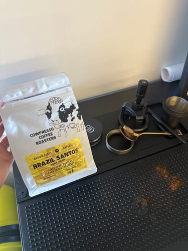 Customer holding a white pouch of Brazil Santos coffee over a black coffee station.