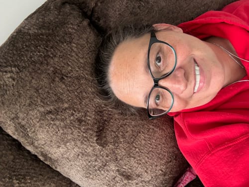 Reviewer in a red hoodie lying down and smiling, showing their Pop On Veneers.