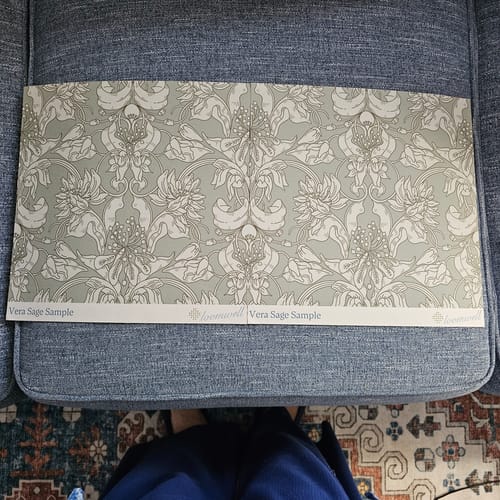 Customer's sample of the Vera Wallpaper in a sage green floral pattern resting on a blue upholstered chair.