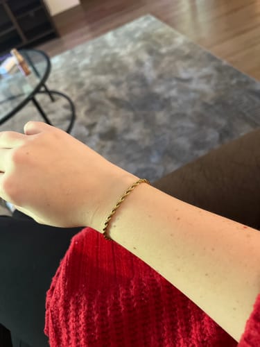 Customer's wrist showing the Twisted 18K Gold Bracelet worn against a chunky red sweater.