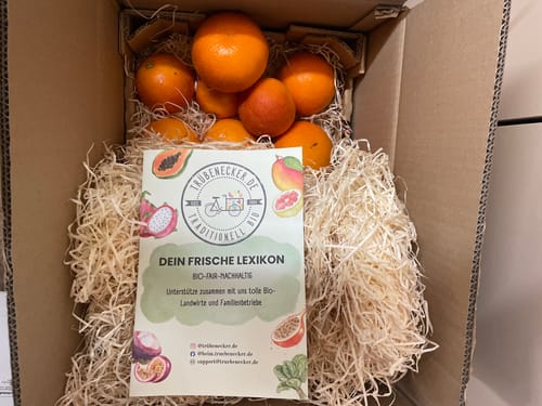 Kunde zeigt die geöffnete Bio Orangen-Mixbox 'Italia'. Die frischen Orangen sind sorgfältig in Holzwolle im Karton verpackt.