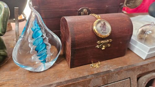 Customer's Memorial Glass Flame with a bright blue ash spiral, displayed on a wooden surface next to a memorial chest.