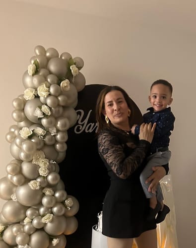 Reviewer wearing the black Nexa Strapless Mini Dress Romper, styled with a separate long-sleeve lace top while holding a child.