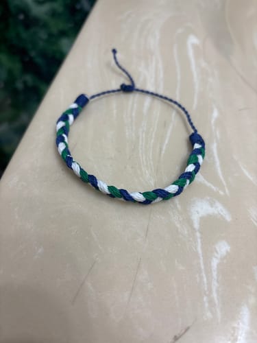 A customer's DAVID Bracelet with woven blue, green, and white strands, laid out on a surface.