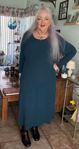 Reviewer standing in a living room wearing the long-sleeved Caroline Ribbed Twirl Dress in Majolica Blue with black boots.