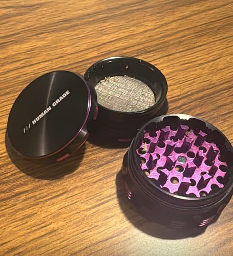 Reviewer's Black Space Herb Grinder disassembled, showing the black and purple parts with the grinding teeth and pollen screen.