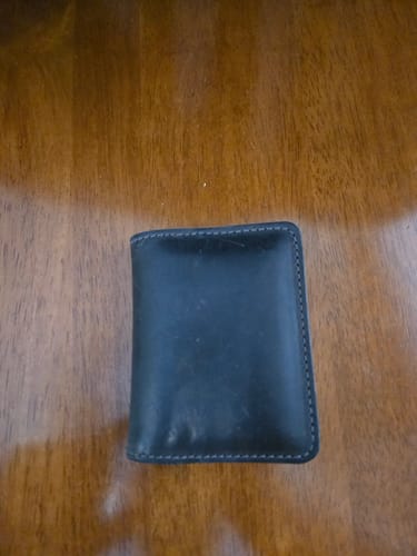 Customer's black Crater Bifold With Zipper shown closed and resting on a wooden table.