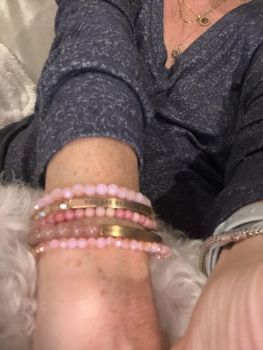 Close-up on a reviewer's wrist showing a stack of pink beaded bracelets, including the bible verse bracelet.