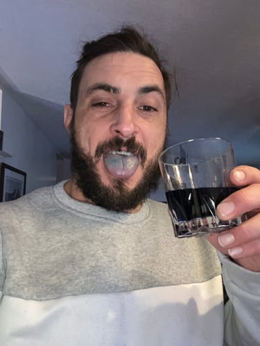 Reviewer shows their blue-stained tongue while holding a glass of Meraki Blu Methylene Blue.