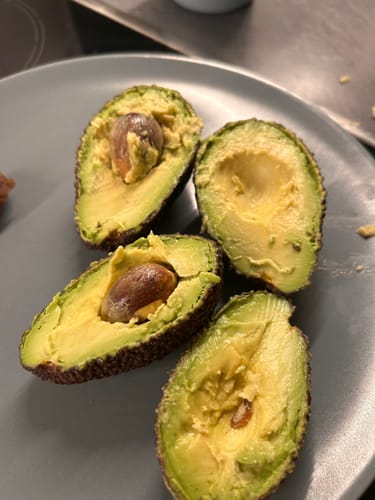 Ein Kunde zeigt zwei aufgeschnittene Reed-Avocados mit cremigem, gelbem Fruchtfleisch auf einem Teller.