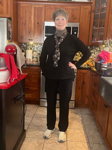Reviewer in a kitchen wearing the black Emerson Straight Leg Pants with a tucked-in top and scarf.