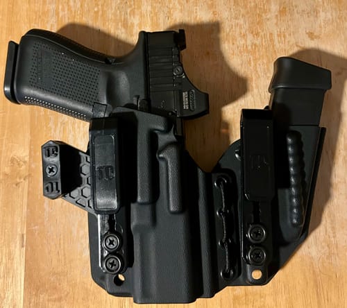 Customer's black AXIS ELITE holster with a handgun inside and an attached magazine holder on a wooden surface.