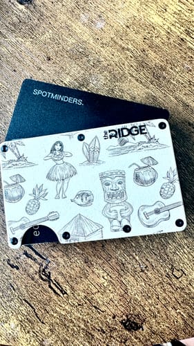Customer's black SPOTMINDERS Tracking Card peeking out from inside a patterned wallet on a wooden surface.