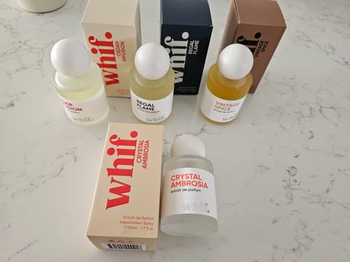 Reviewer's collection of four perfumes, with the Crystal Ambrosia bottle and box shown in the foreground on a marble surface.