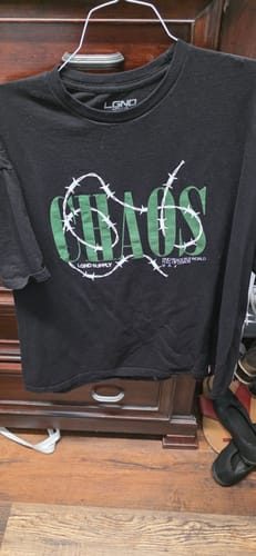 Customer's black t-shirt with a green 'Chaos' graphic from the mystery box, shown on a hanger.