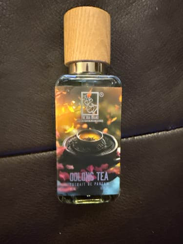 Reviewer's Oolong Tea perfume bottle with a wooden cap, resting on a dark leather surface.
