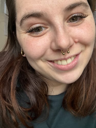 Nahaufnahme einer lächelnden Kundin, die ihre langen Wimpernextensions zeigt, die mit dem BOND GIRL+ Wimpernkleber angebracht wurden.