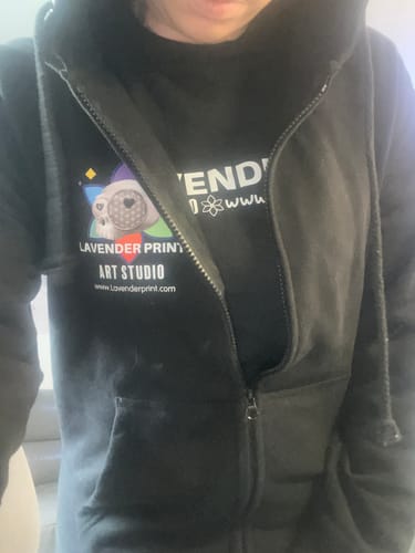 A reviewer wearing the black ladies zip hoodie, partially unzipped, showing the custom logo printed on the left chest.