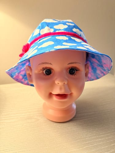 Reviewer's bucket hat made from the blue White Clouds Fabric, shown on a mannequin head with a bright pink ribbon.