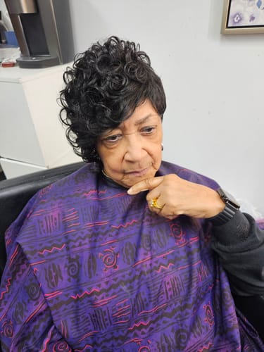Reviewer in a salon chair wearing the short, curly Cynthia human hair wig after it was styled.