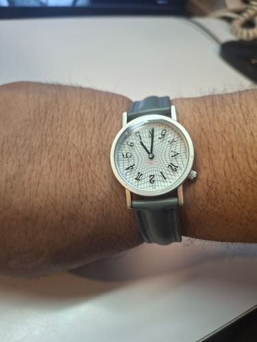 Cliente mostrando su reloj análogo Relatividad de Einstein con correa de cuero en su muñeca.