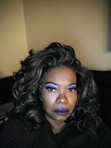 Reviewer showing off the voluminous, curly JOVIE wig in a dark color with highlights.