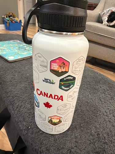 Customer's white Canada Bottle with a black lid, shown with several colorful destination stickers applied.