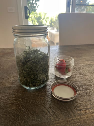 Customer shows home grown produce, dried herbs and fresh strawberries, in two different sized mason jars ready for sealing.