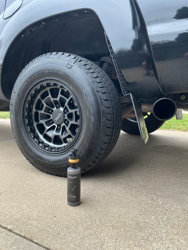 Customer's photo showing a clean, dark tire on their truck with the bottle of Blackline product in front.